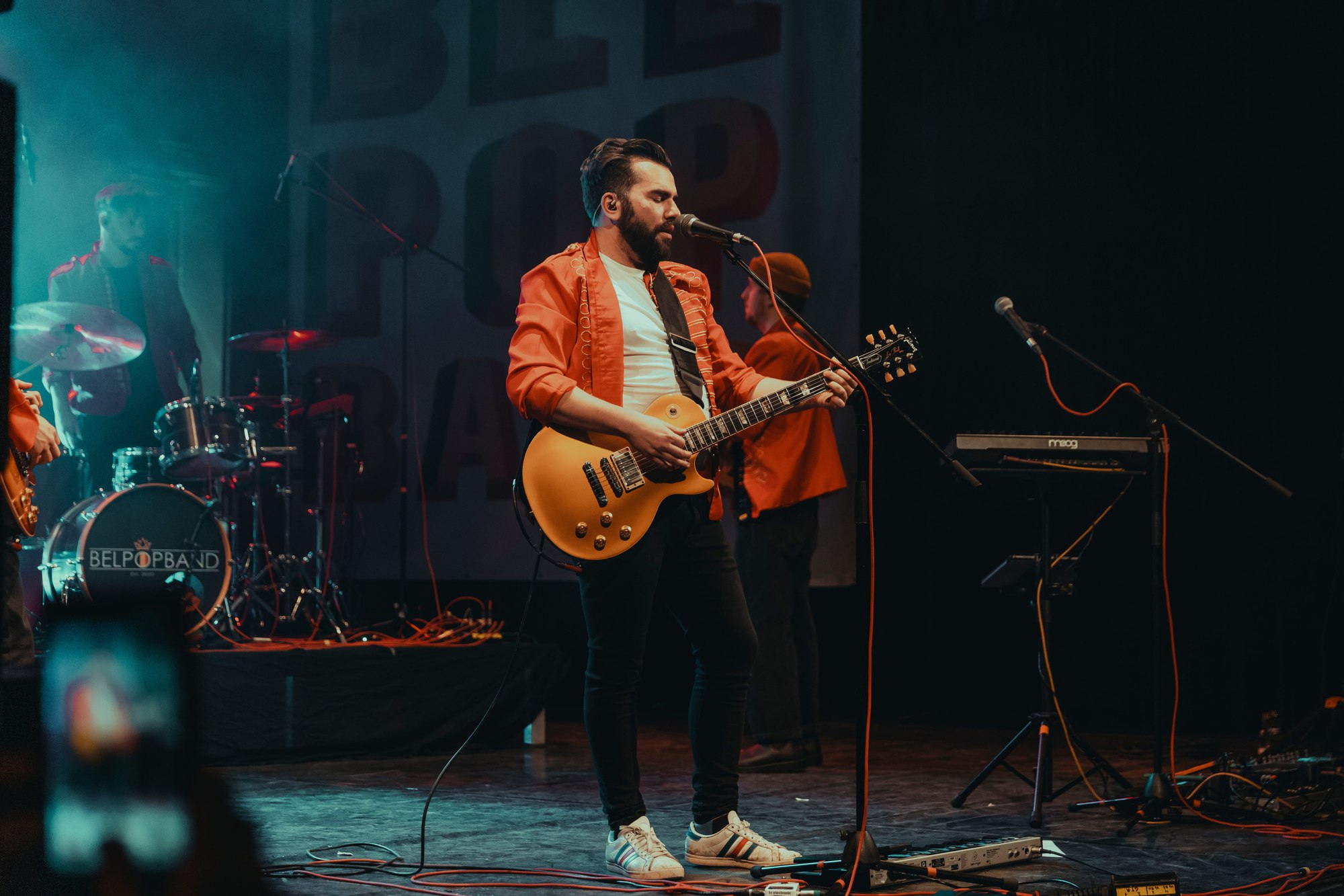 De Belpopband tijdens een live optreden, zanger met gitaar op het podium
